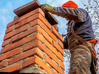 Mason setting a cap stone atop a chimney near the coast