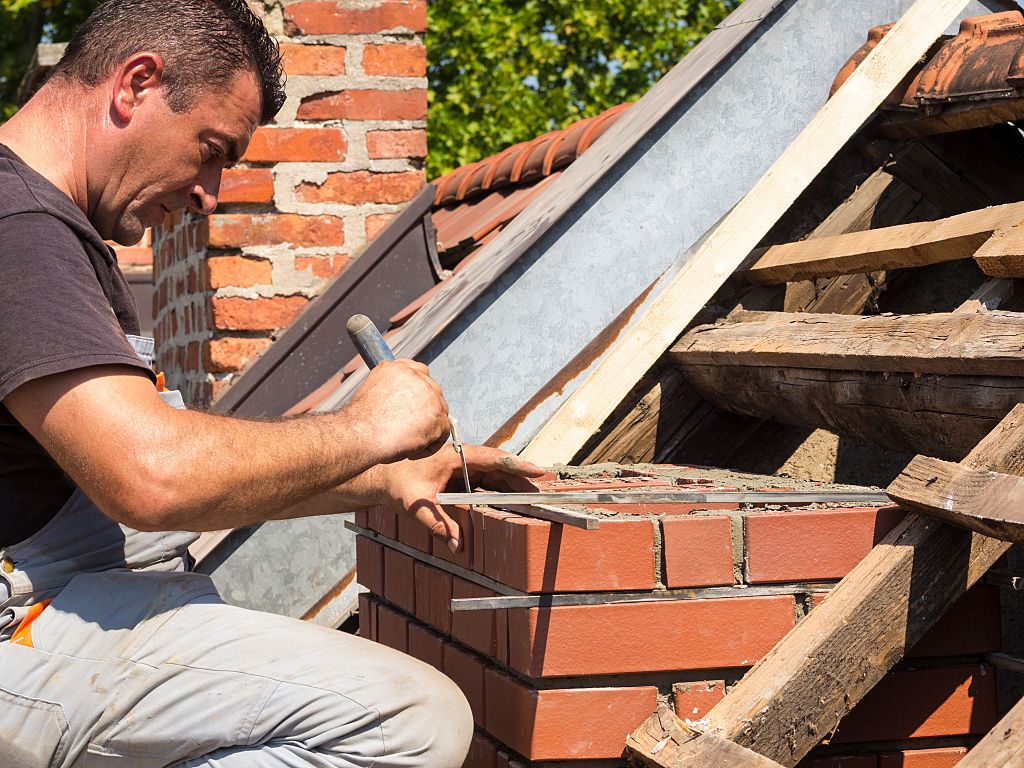 Mason laying courses on a rebuilt brick chimney near Redondo Beach